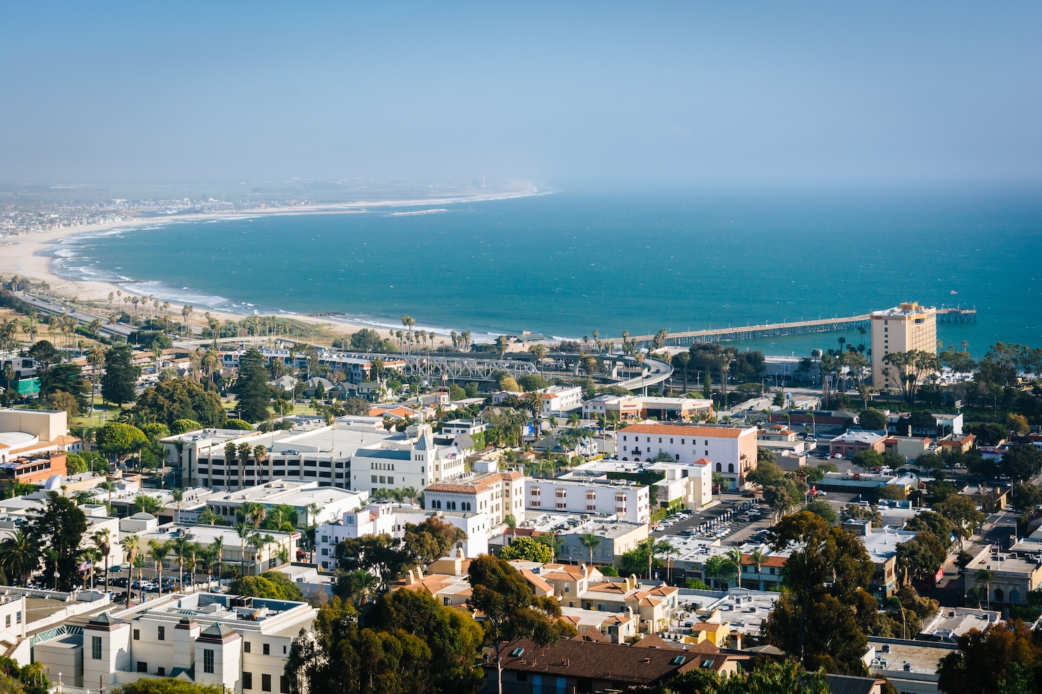 Aerial view of Ventura cityscape with coastline, beach, and blue ocean under clear sky, featuring iconic pier.